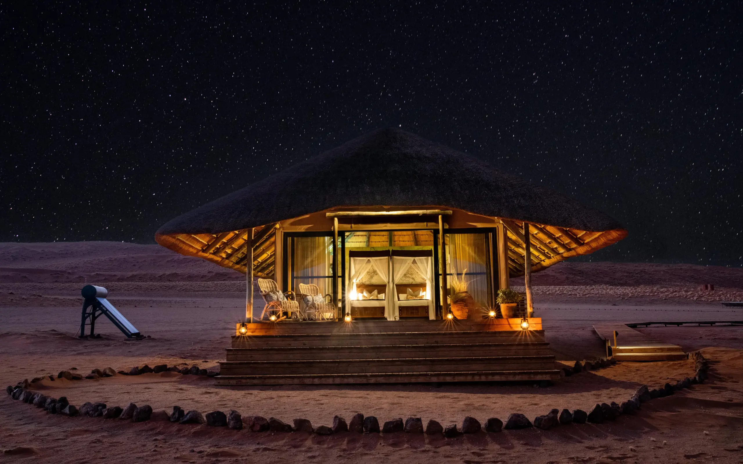 Illuminated glamping tent with stone circle in desert landscape at night, Kwessi Dunes, NamibRand Private Reserve, Namibia
