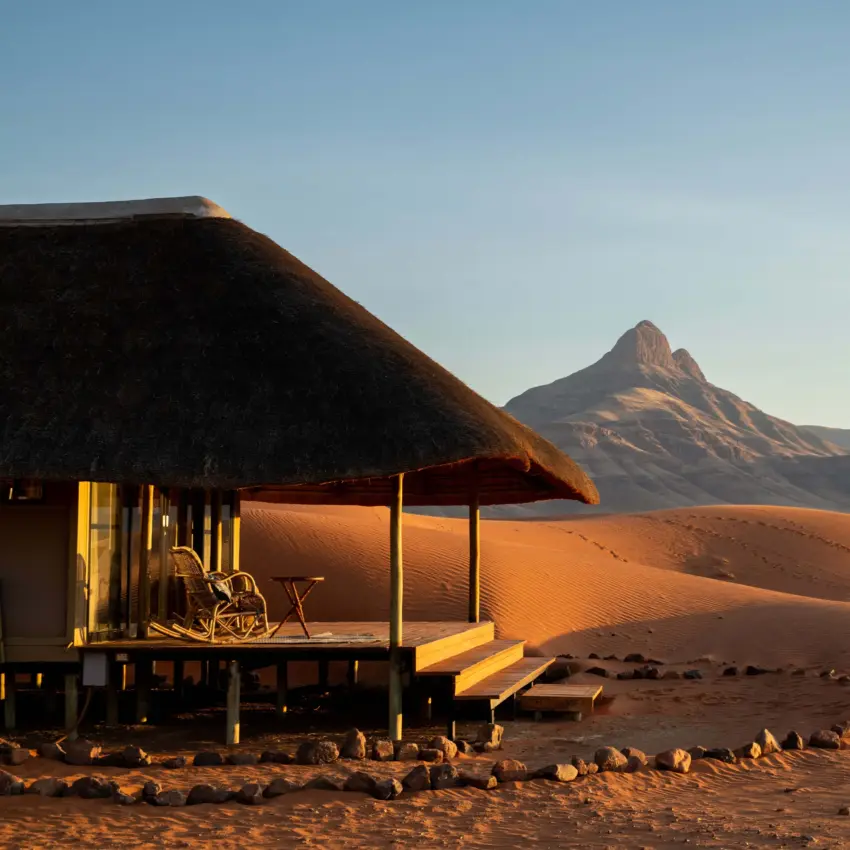 Thatched-roof desert lodge with mountain view at sunset, Kwessi Dunes, NamibRand Private Reserve, Namibia