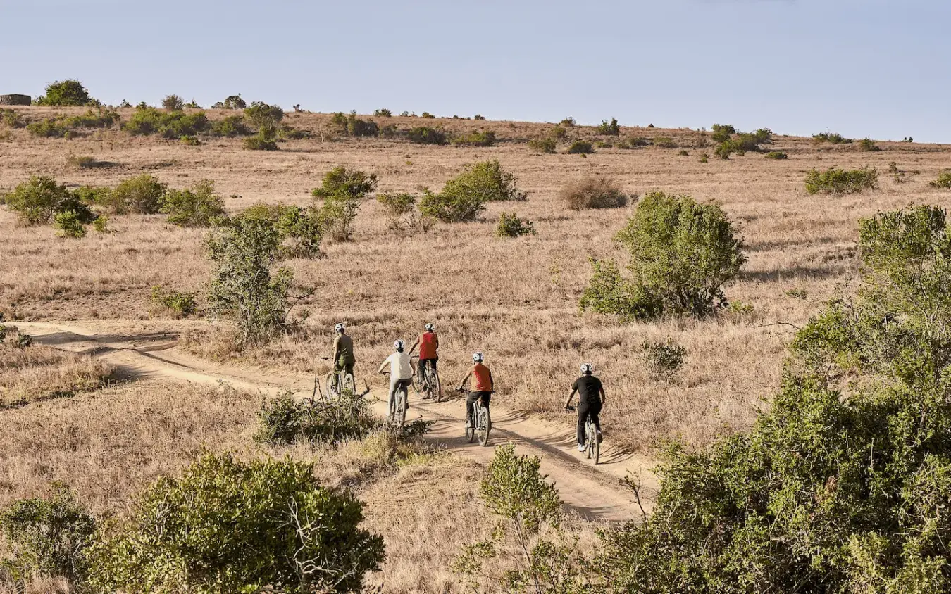 Group of cyclists riding on dirt path through dry savanna, Lengishu House, Laikipia Highlands, Kenya