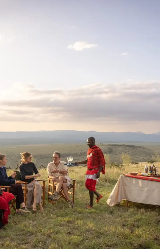 Maasai guide serving drinks to guests at outdoor safari dinner with valley views, Lewa House, Laikipia Highlands, Kenya