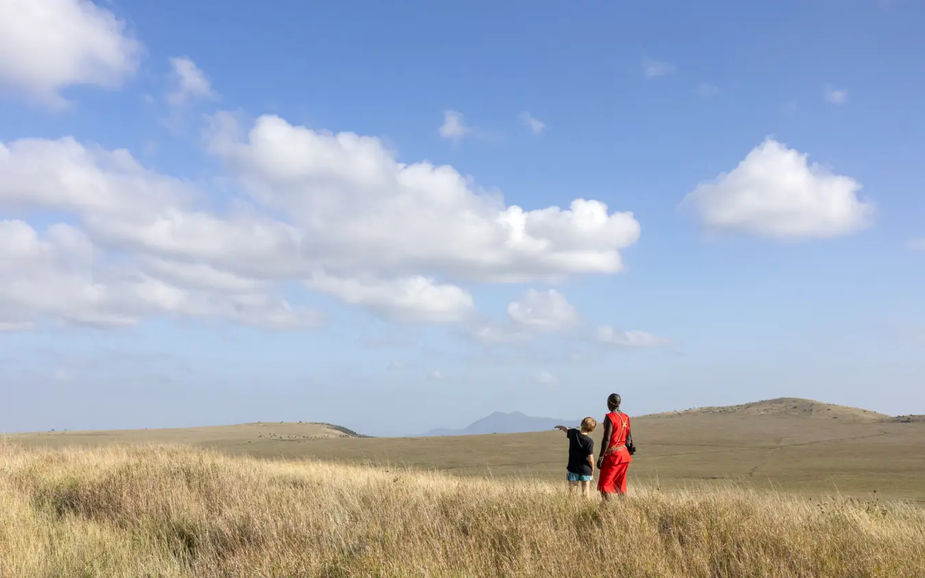 Two people walking through grassland with distant hills and clouds, Lewa House, Laikipia Highlands, Kenya