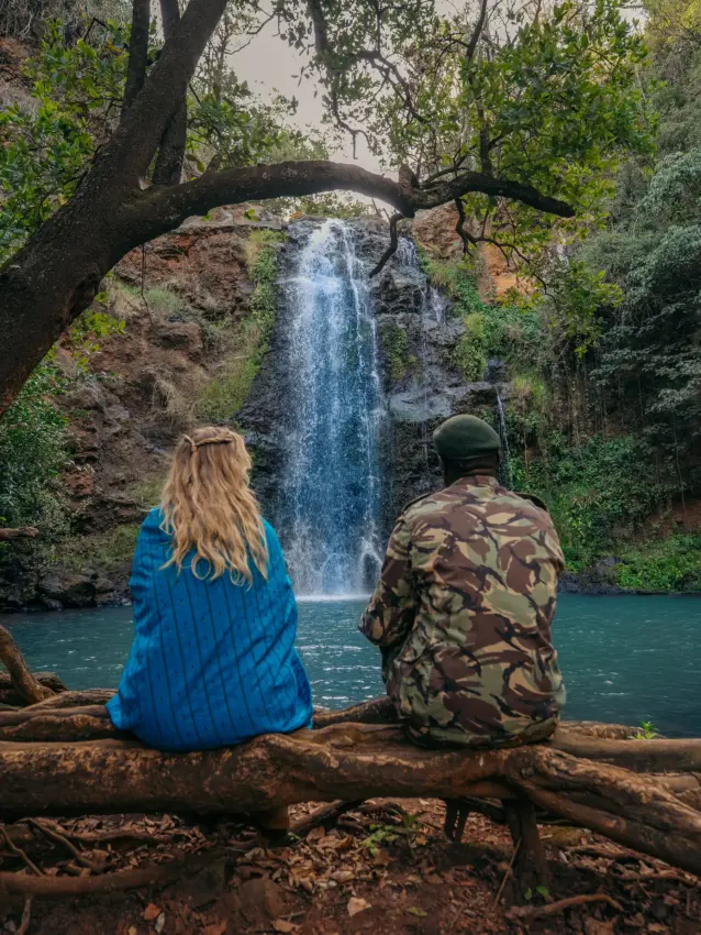 Two guests viewing waterfall from log beside turquoise pool, Lewa House, Laikipia Highlands, Kenya