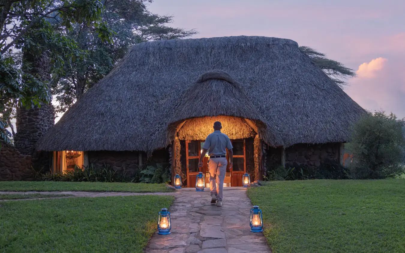 Guest approaching illuminated thatched lodge at dusk with lantern pathway, Lewa House, Laikipia Highlands, Kenya