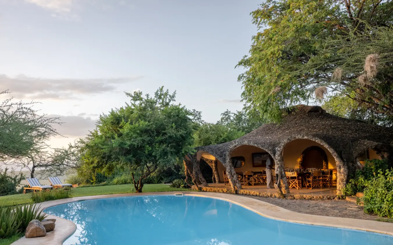 Swimming pool with stone bungalows at sunset overlooking savanna landscape, Lewa House, Laikipia Highlands, Kenya
