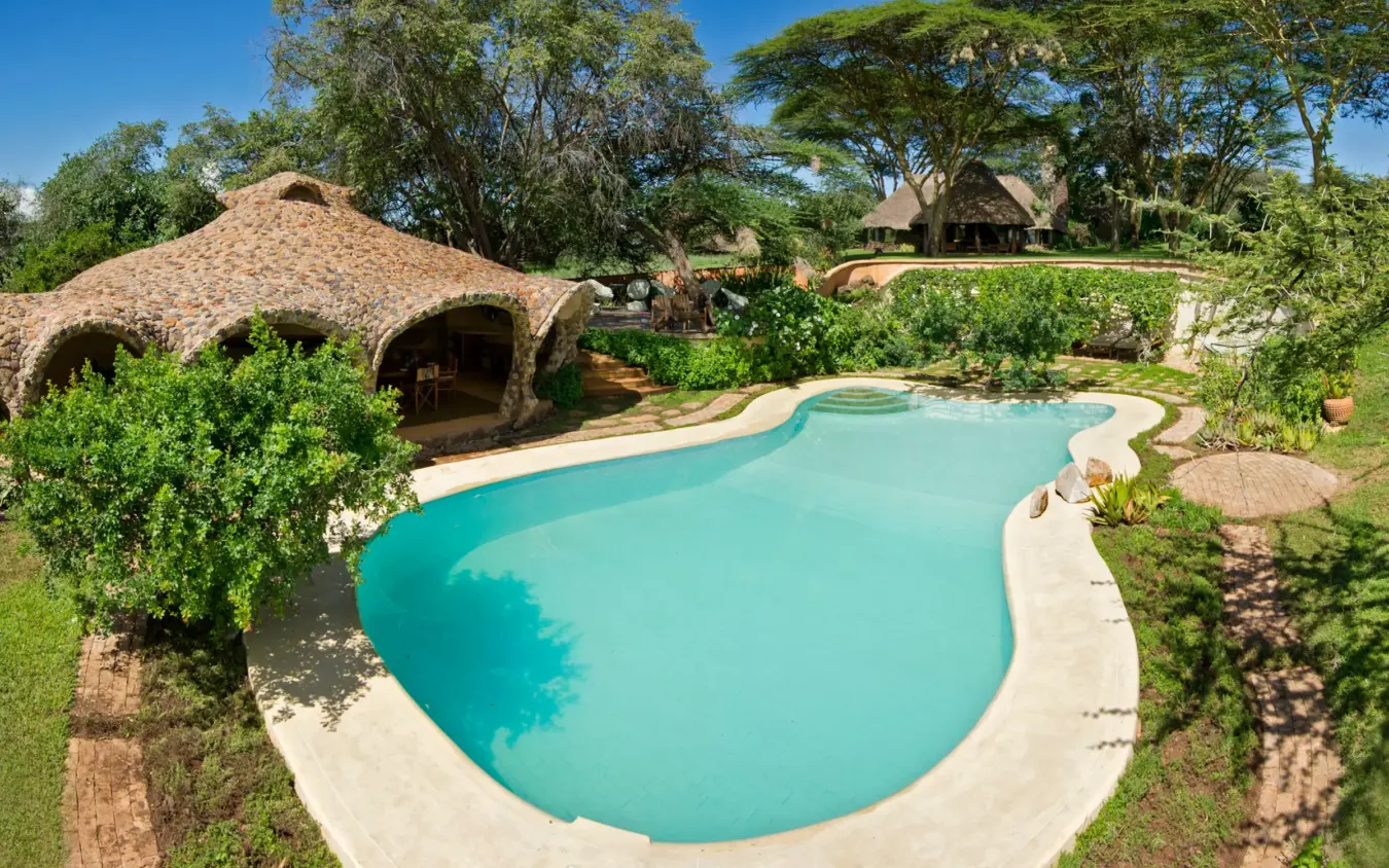 Turquoise swimming pool with thatched-roof bungalow in savanna landscape, Lewa House, Laikipia Highlands, Kenya