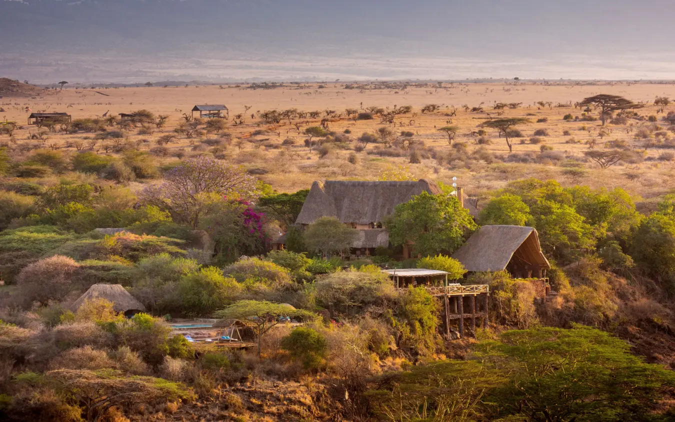 Luxury lodge with thatched roofs nestled in savanna landscape with waterhole, Lewa Wilderness, Laikipia Highlands, Kenya