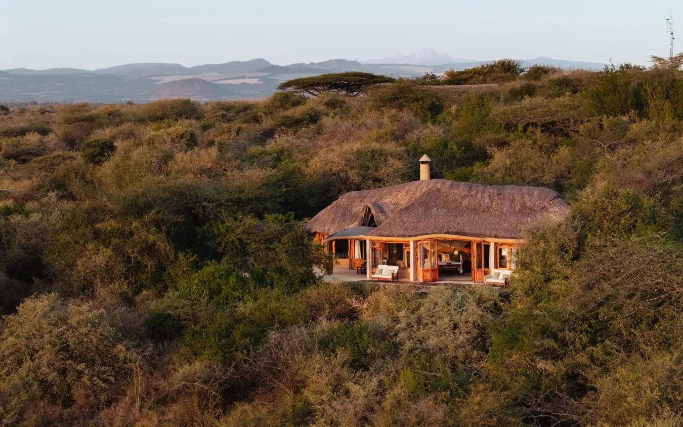 Thatched-roof lodge nestled among acacia trees in rolling savanna landscape, Lewa Wilderness, Laikipia Highlands, Kenya