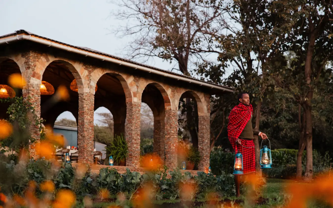 Man in traditional red shawl standing by colonial stone archway at dusk, Lewa Wilderness, Laikipia Highlands, Kenya