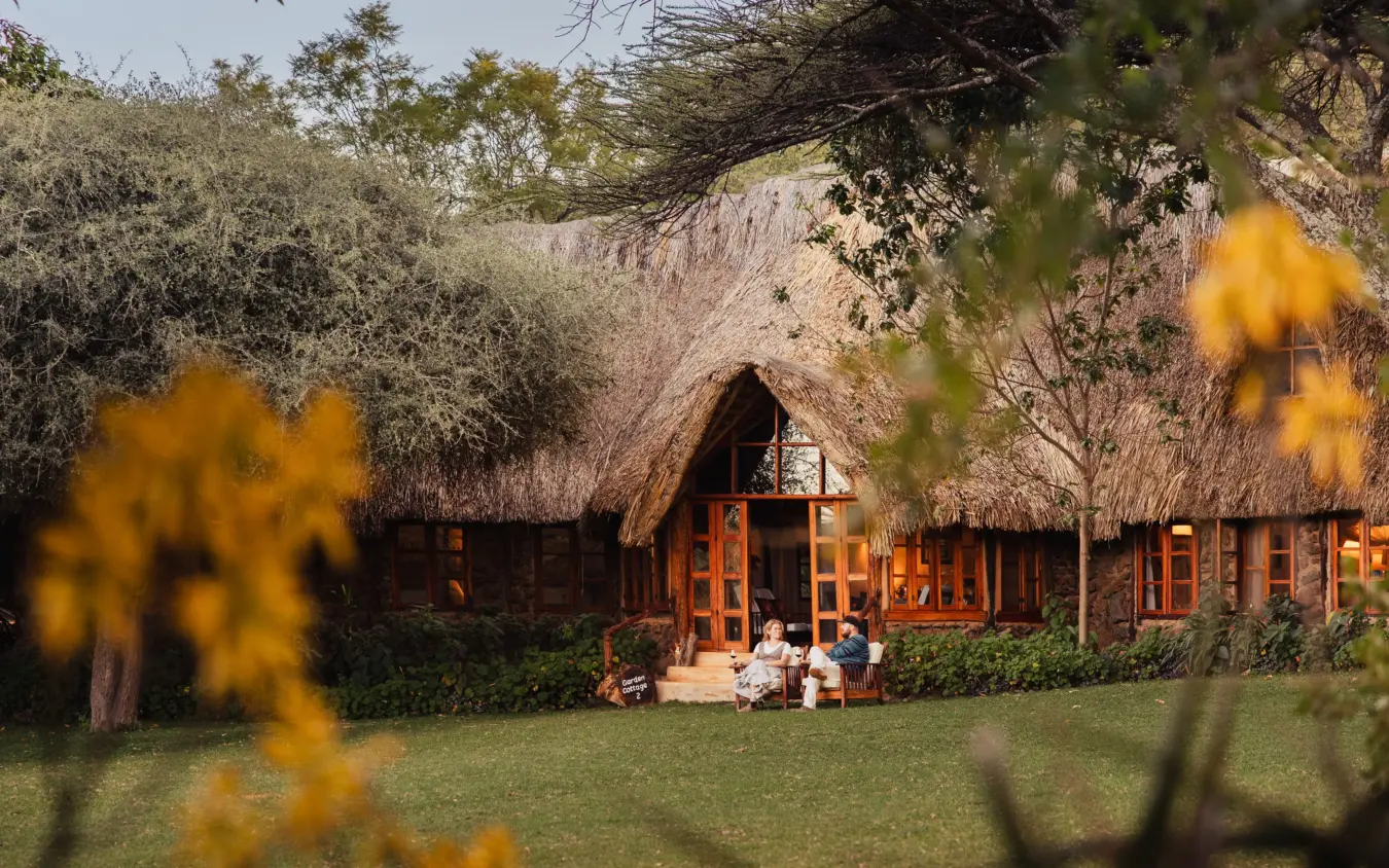 Thatched-roof lodge with wooden deck and guests relaxing on manicured lawn, Lewa Wilderness, Laikipia Highlands, Kenya