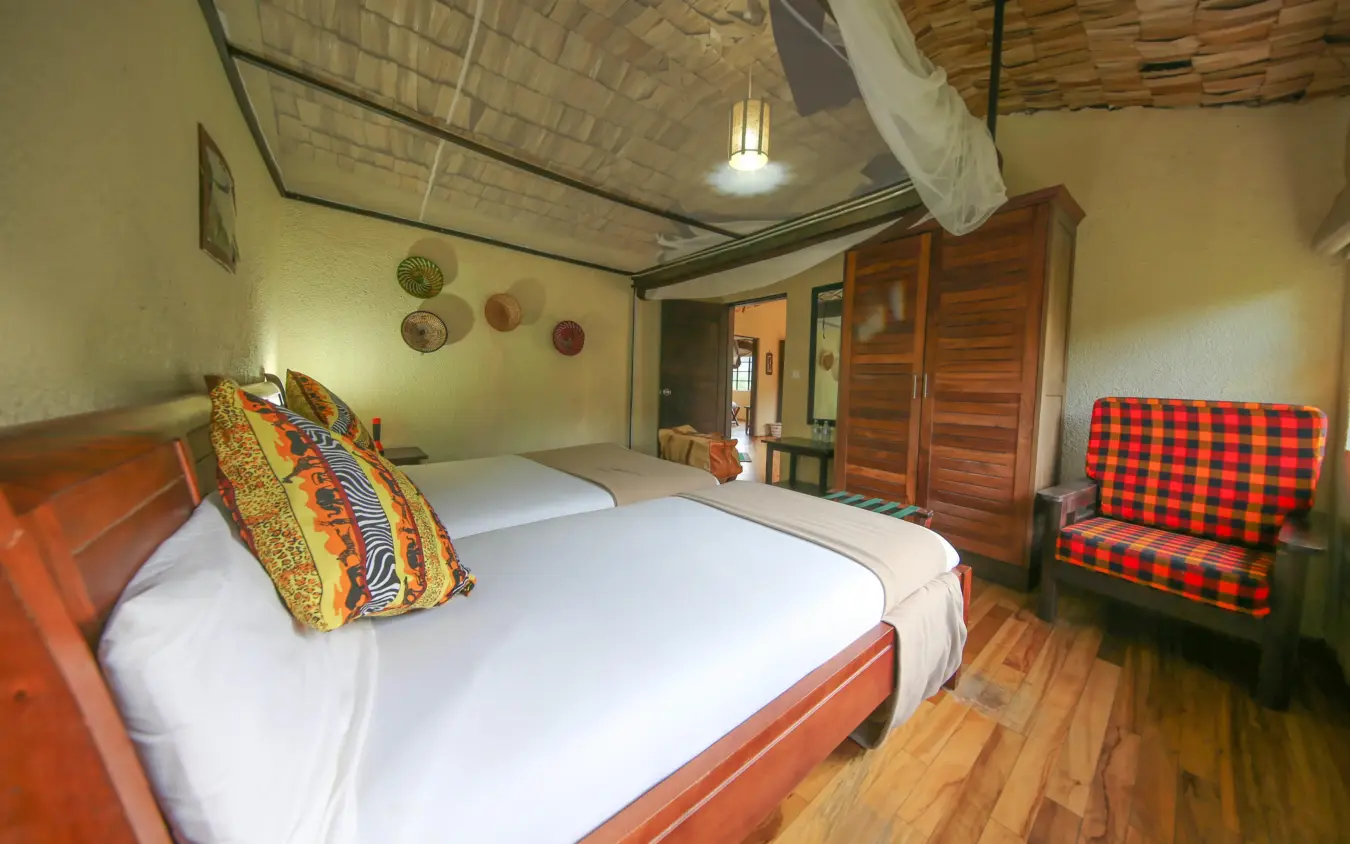 Spacious bedroom with wooden bed and red patterned seating, Mahogany Springs, Bwindi Impenetrable Forest, Uganda