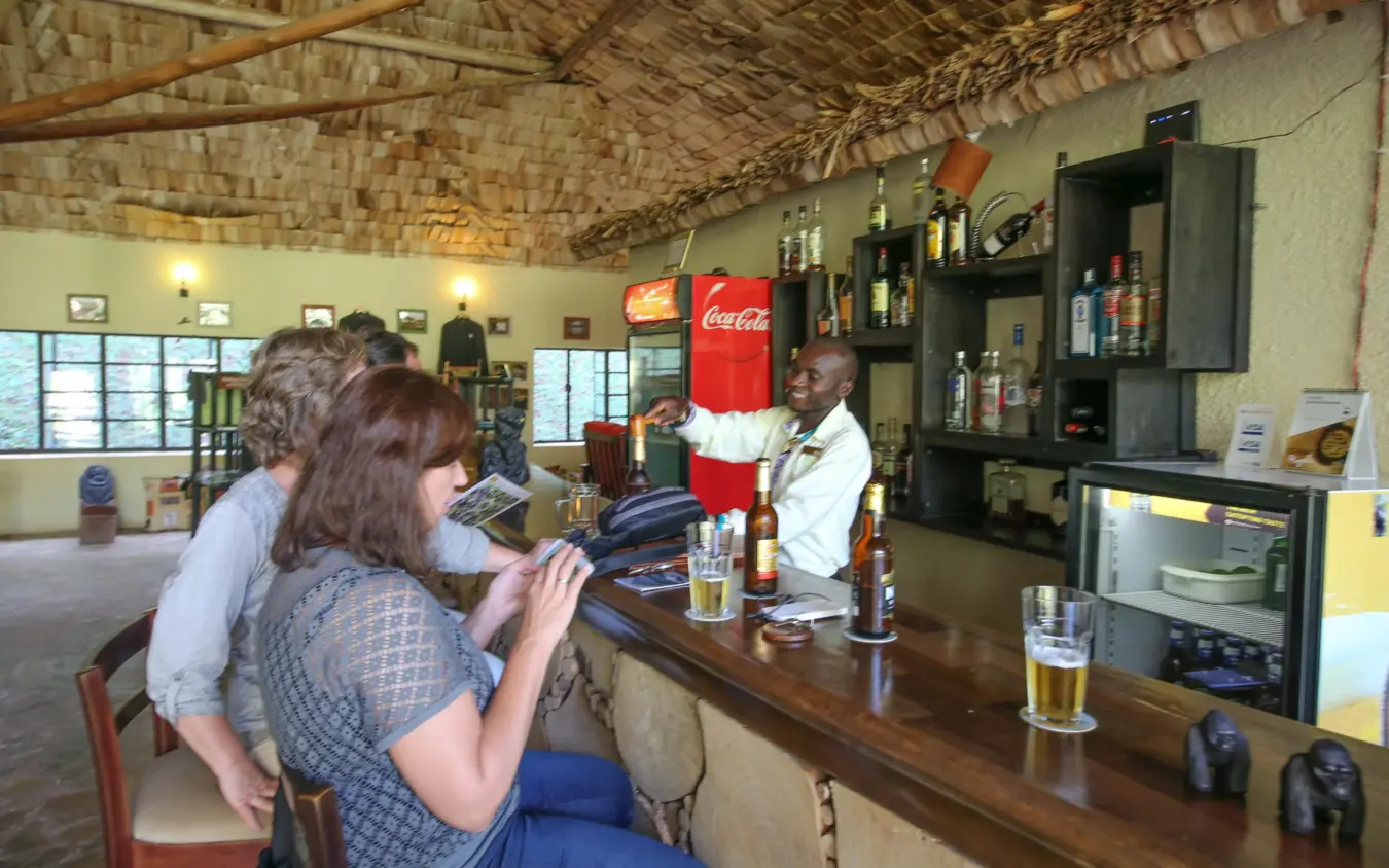 Guest at bar counter with bartender in rustic lodge, Mahogany Springs, Bwindi Impenetrable Forest, Uganda