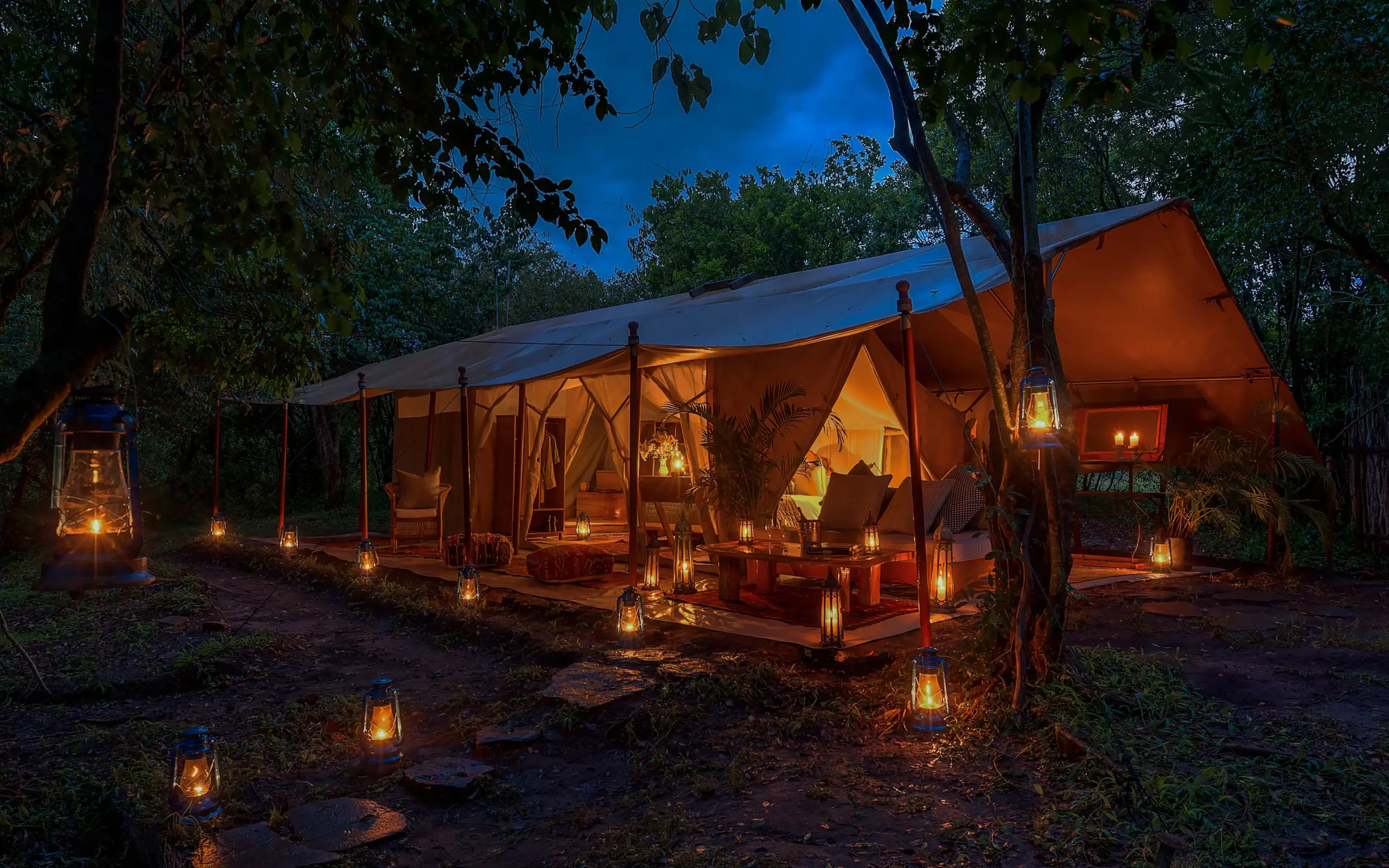 Illuminated safari tent camp nestled among trees at dusk, Naibor Camp, Maasai Mara, Kenya