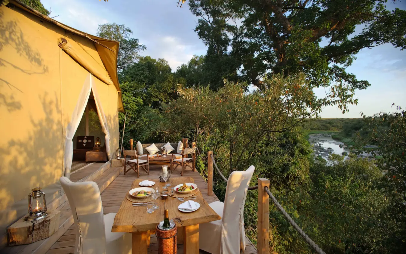 Glamping tent deck with dining setup overlooking river, Naibor Camp, Maasai Mara, Kenya