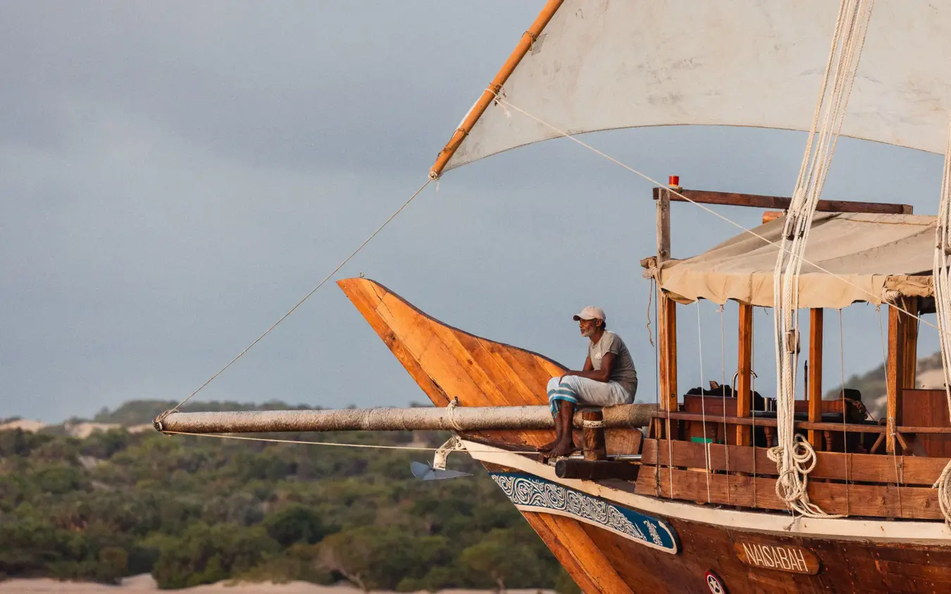 Wooden sailing dhow with crew member on deck overlooking coastal landscape, NaiSabah, Lamu Archipelago, Kenya