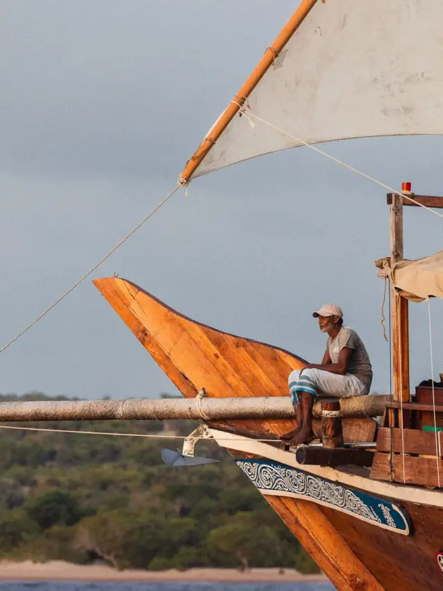 Fisherman on wooden boat with orange sail and rope rigging, NaiSabah, Lamu Archipelago, Kenya