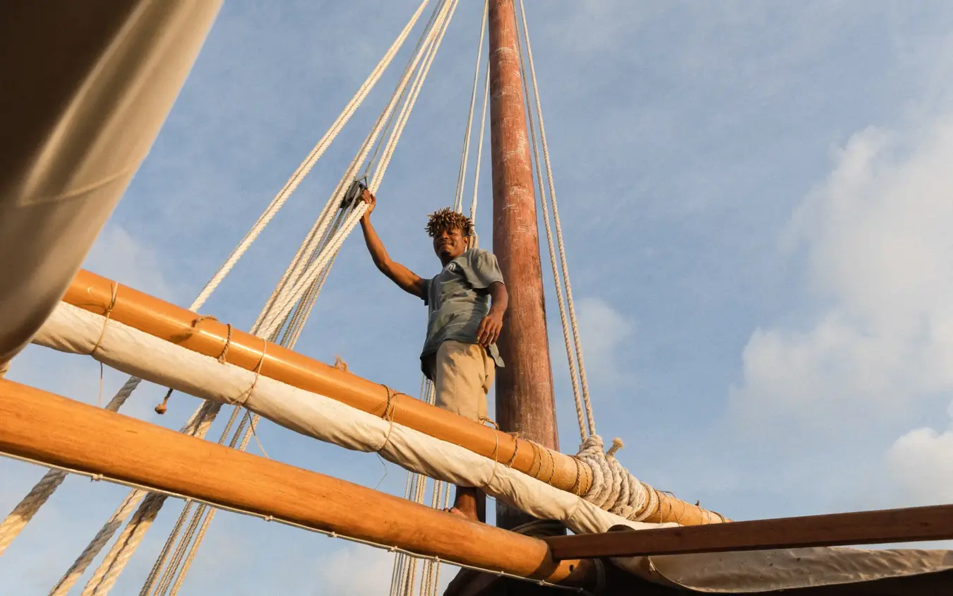 Crew member climbing wooden mast on traditional sailing vessel, NaiSabah, Lamu Archipelago, Kenya