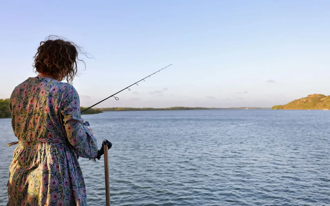Woman fishing from shoreline at dusk with distant islands, NaiSabah, Lamu Archipelago, Kenya