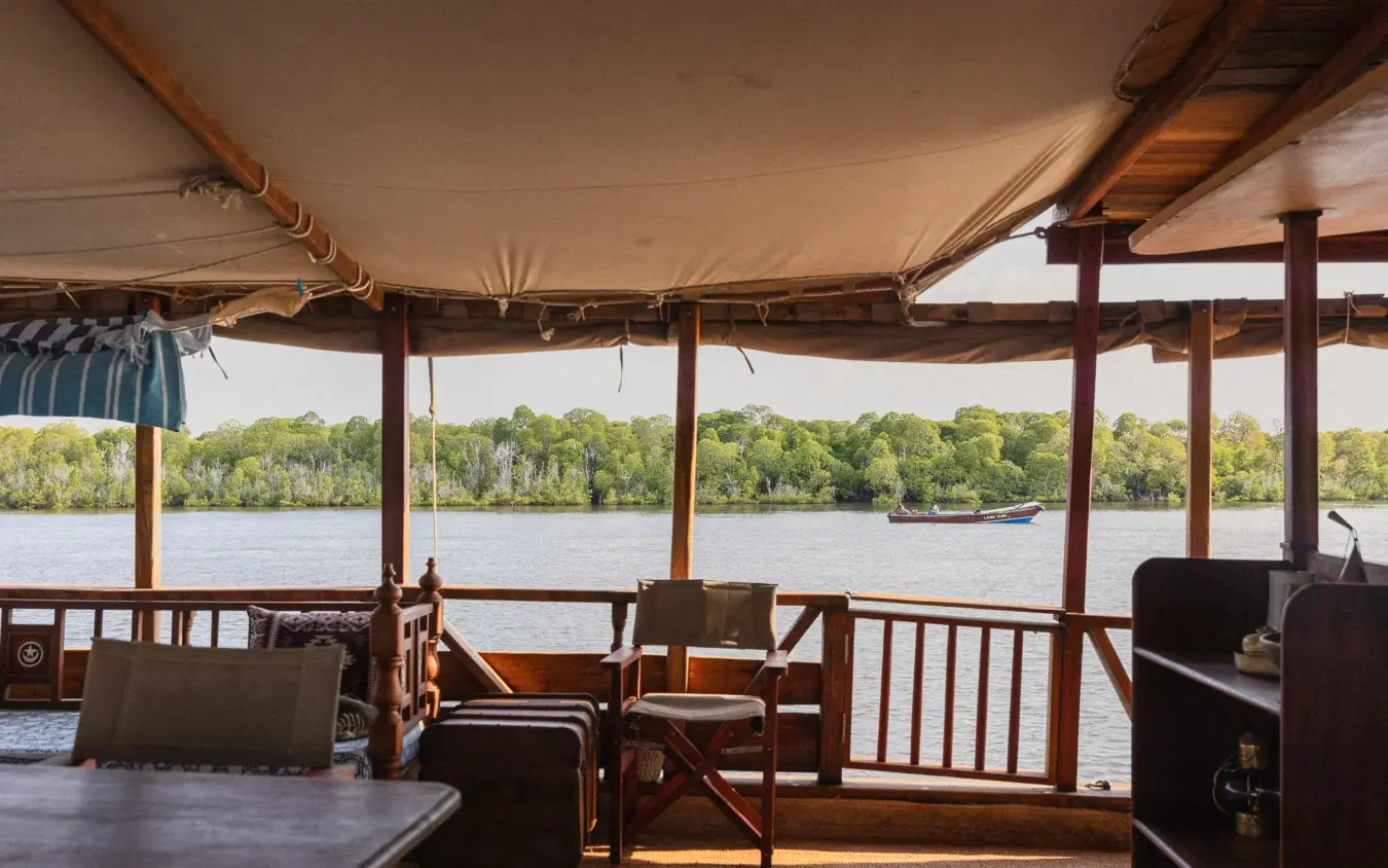 Wooden river cruise boat with shaded deck overlooking waterfront forest, NaiSabah, Lamu Archipelago, Kenya