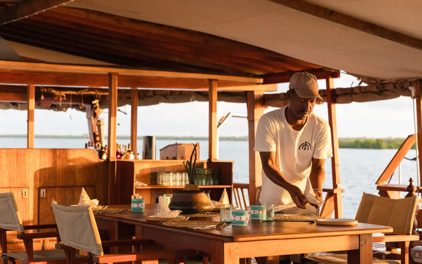 Man preparing meal in open-sided riverside lodge with water views, NaiSabah, Lamu Archipelago, Kenya