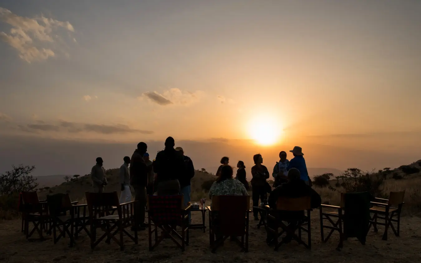 Group gathered around campfire at sunset in savanna landscape, Ndutu Mobile Tented Camp, Serengeti National Park, Tanzania