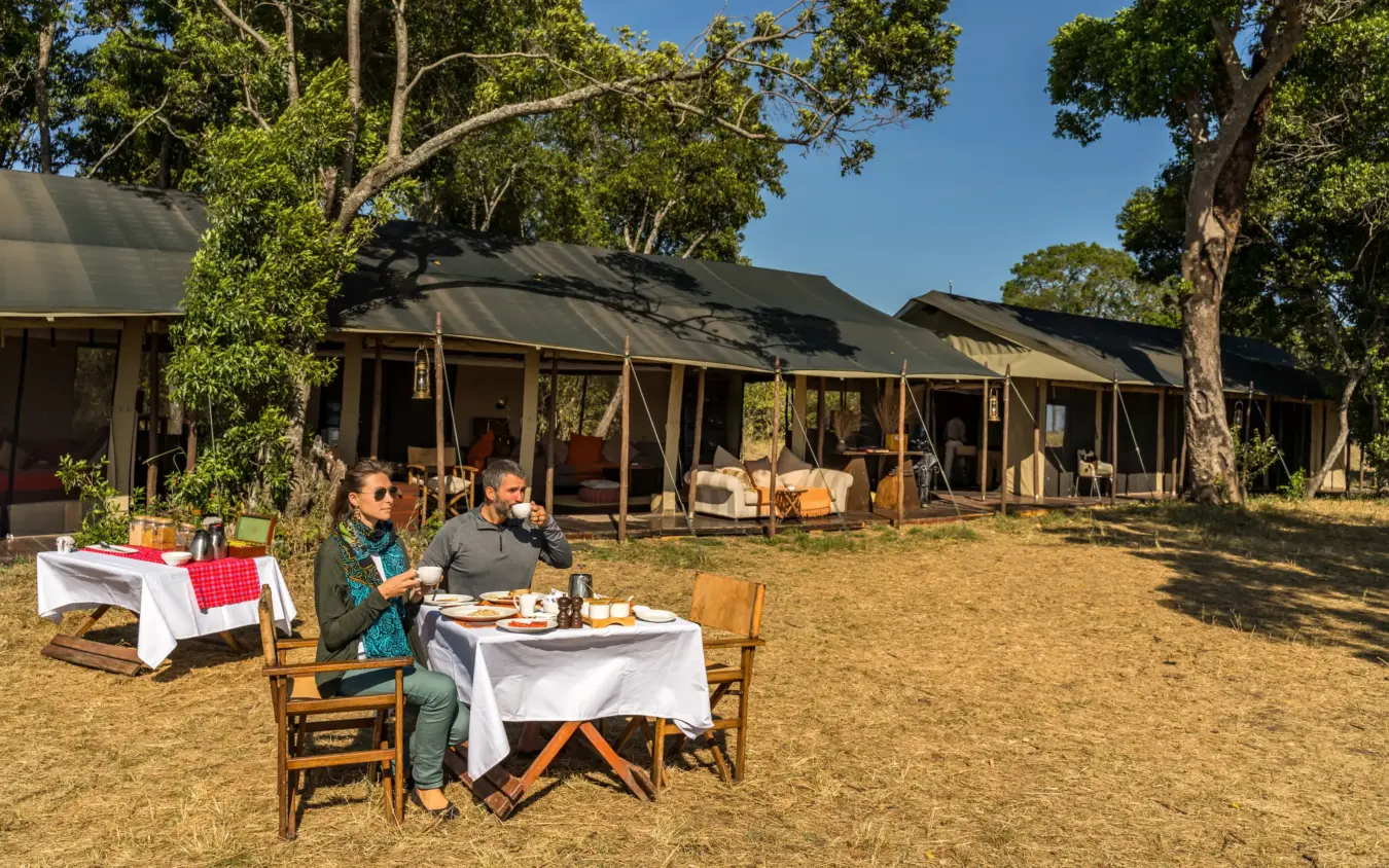 Guests dining at table under acacia trees at safari camp, Ndutu Mobile Tented Camp, Serengeti National Park, Tanzania