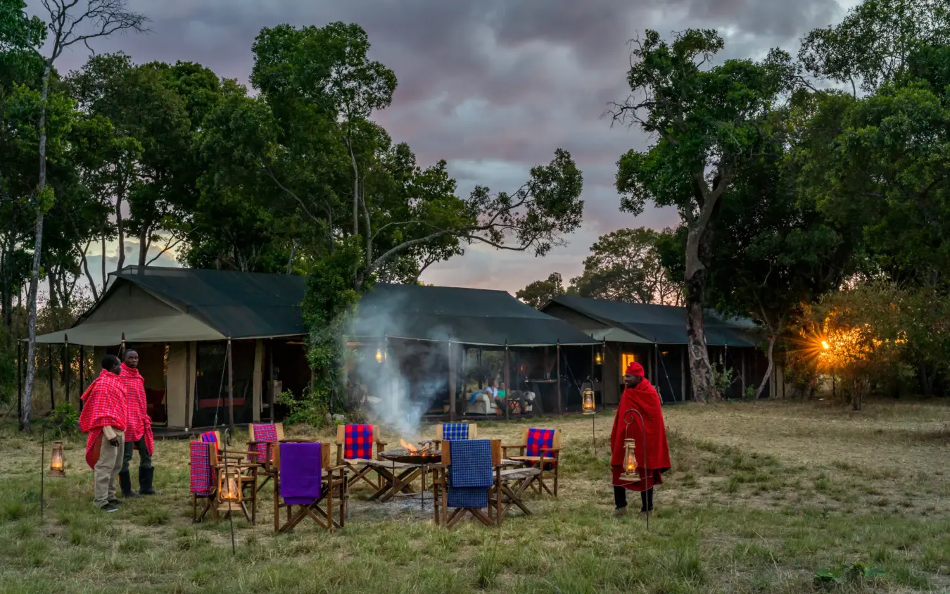 Campfire gathering at safari lodge with guests in traditional red wraps at dusk, Ndutu Mobile Tented Camp, Serengeti National Park, Tanzania