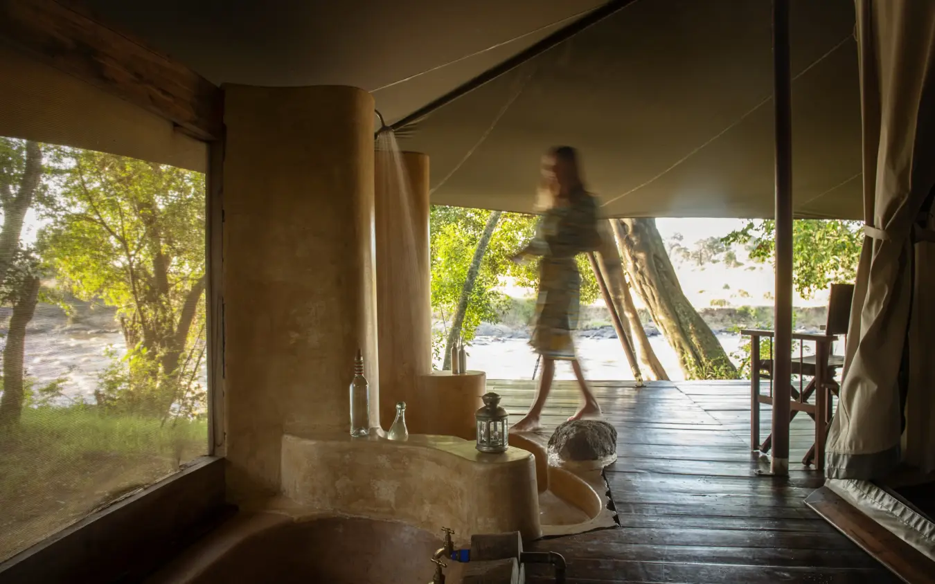 Luxury safari lodge bathroom with freestanding tub and river views through open tent, Ngare Serian, Maasai Mara, Kenya