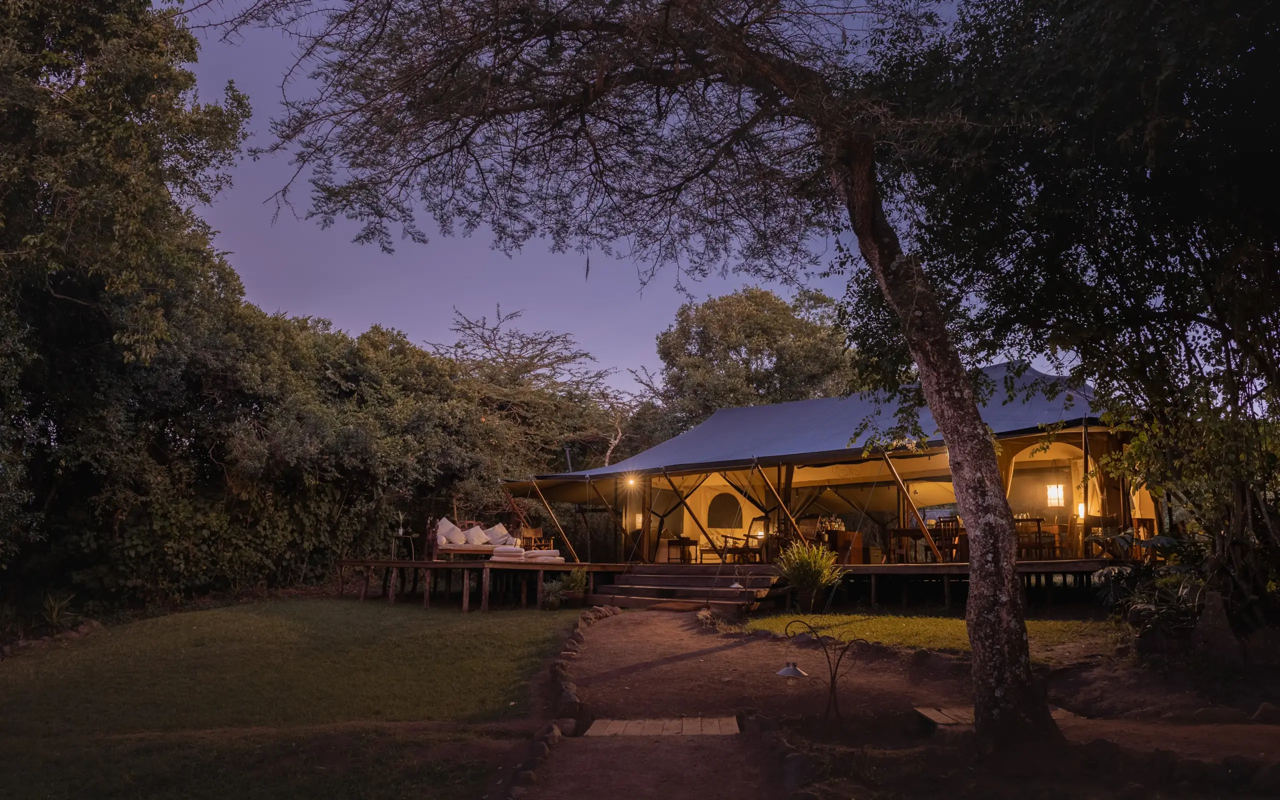 Illuminated safari lodge beneath acacia trees at dusk, Ngare Serian, Maasai Mara, Kenya