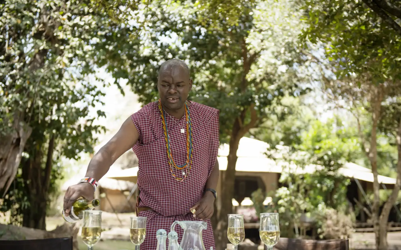 Man pouring wine at outdoor table under tree canopy, Ngare Serian, Maasai Mara, Kenya