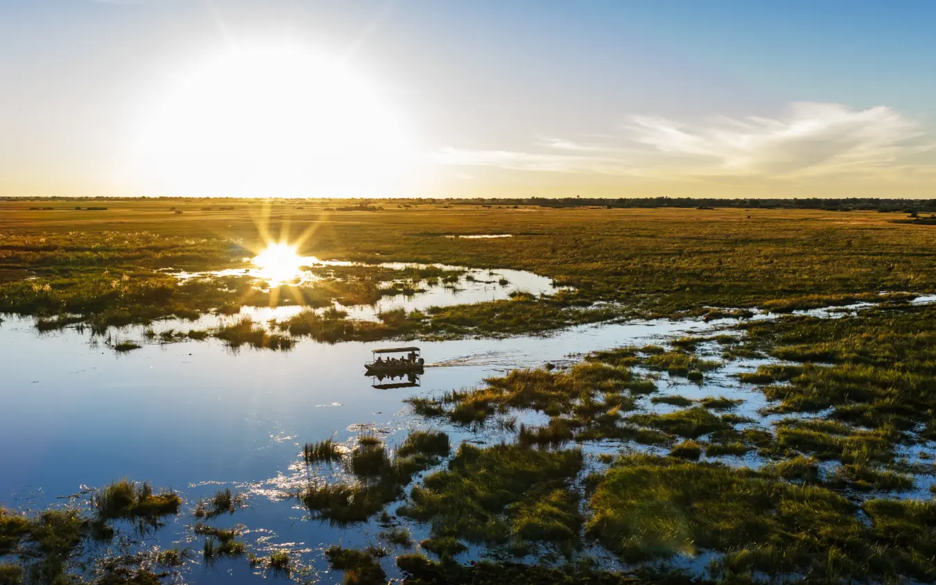 Safari vehicle navigating through shallow waterways in wetland landscape at sunset, Nkasa Linyanti, Zambezi Region, Namibia