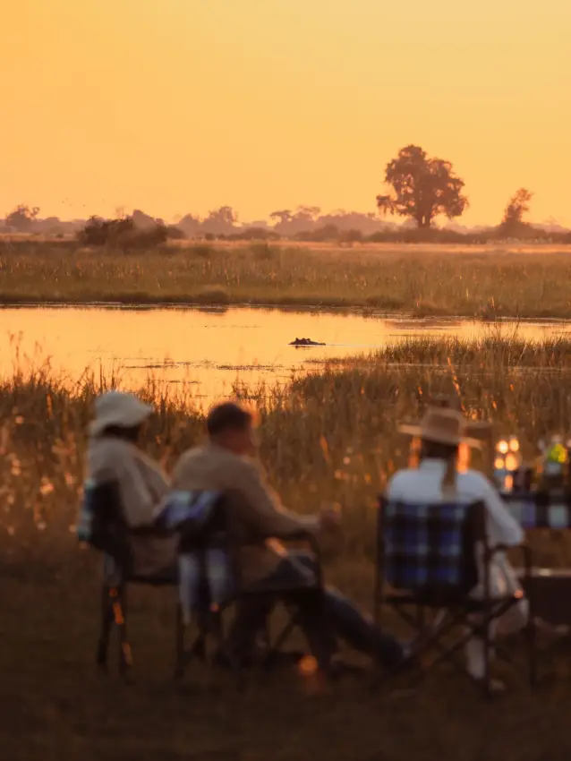 Guests watching sunset from camp overlooking wetland with wildlife, Nkasa Linyanti, Zambezi Region, Namibia
