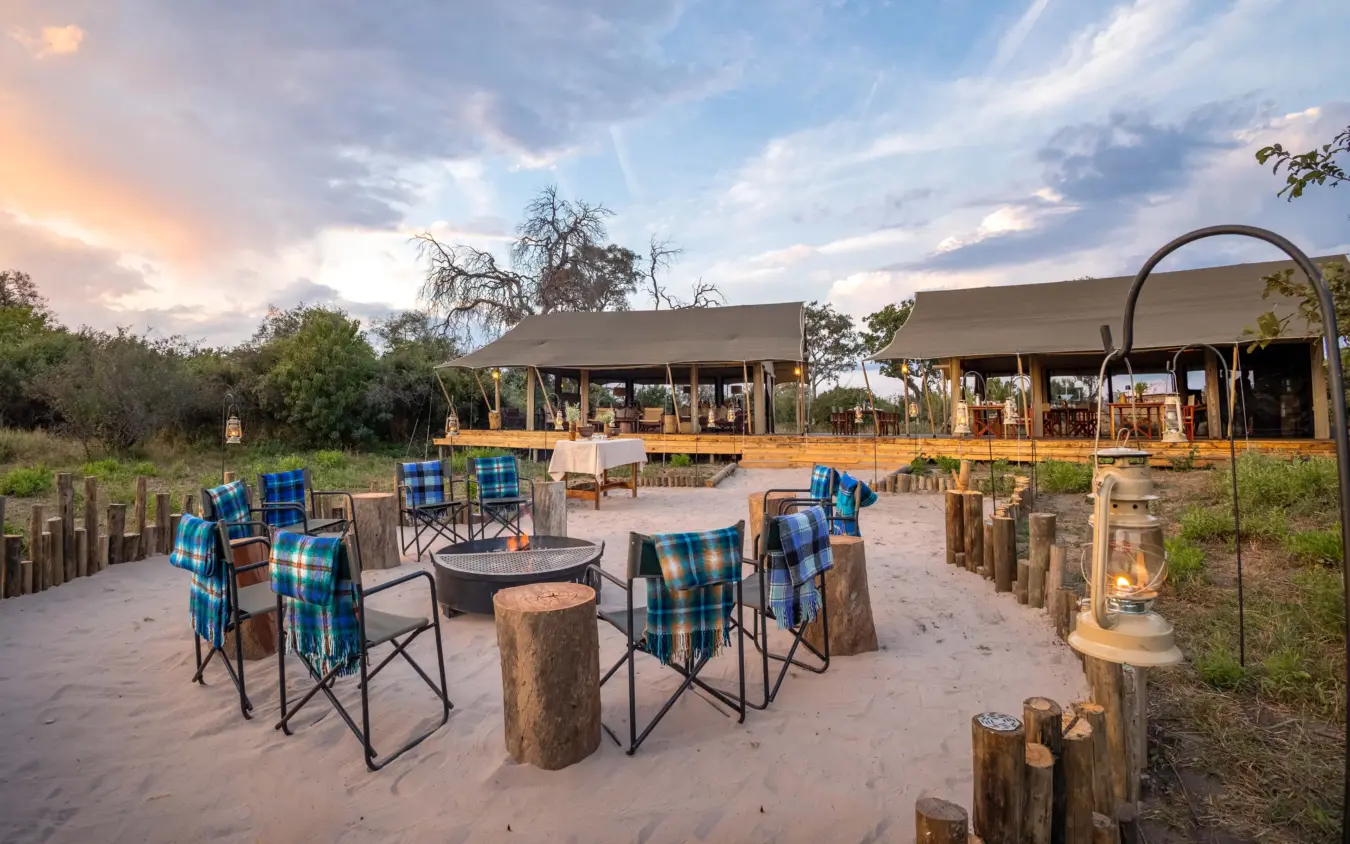 Outdoor lounge area with campfire seating and safari tents at dusk, Nkasa Linyanti, Zambezi Region, Namibia