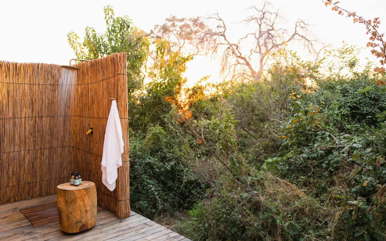 Outdoor shower enclosure with white towel overlooking savanna woodland at sunset, Nkasa Linyanti, Zambezi Region, Namibia
