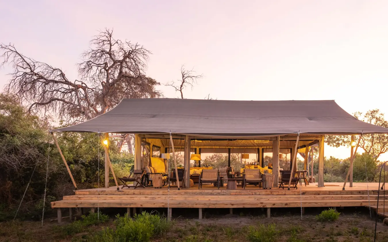Luxury safari lodge with illuminated interior at dusk surrounded by trees, Nkasa Linyanti, Zambezi Region, Namibia