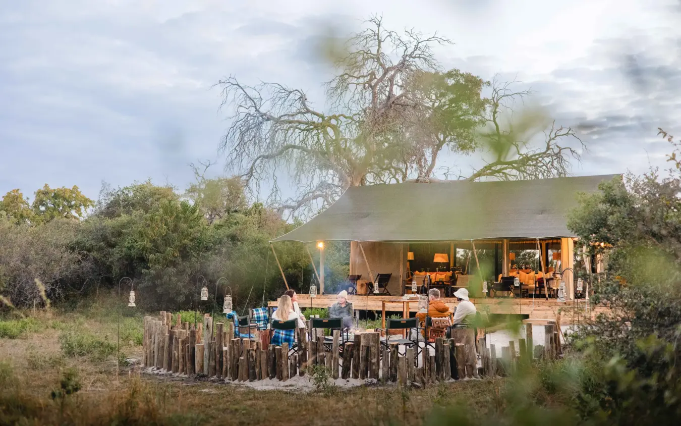 Guests dining at open-air safari lodge at dusk with wildlife surrounding, Nkasa Linyanti, Zambezi Region, Namibia