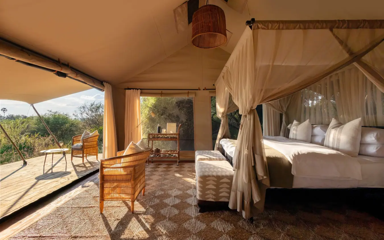 Luxury safari tent interior with four-poster bed and open-air deck overlooking landscape, Nkasa Linyanti, Zambezi Region, Namibia