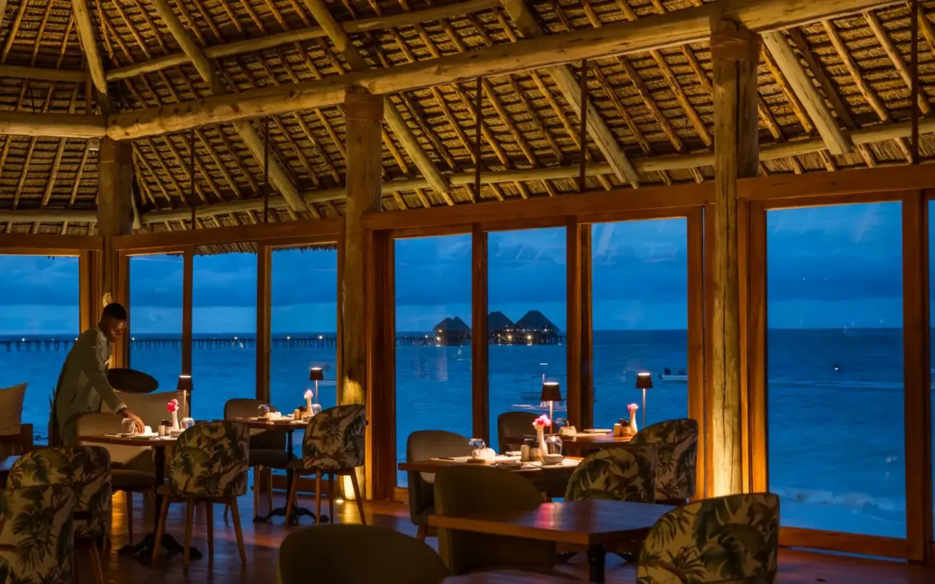 Overwater restaurant pavilion with diners at tables overlooking calm lagoon at dusk, Ocean Boutique Hotel, Zanzibar & Pemba, Tanzania