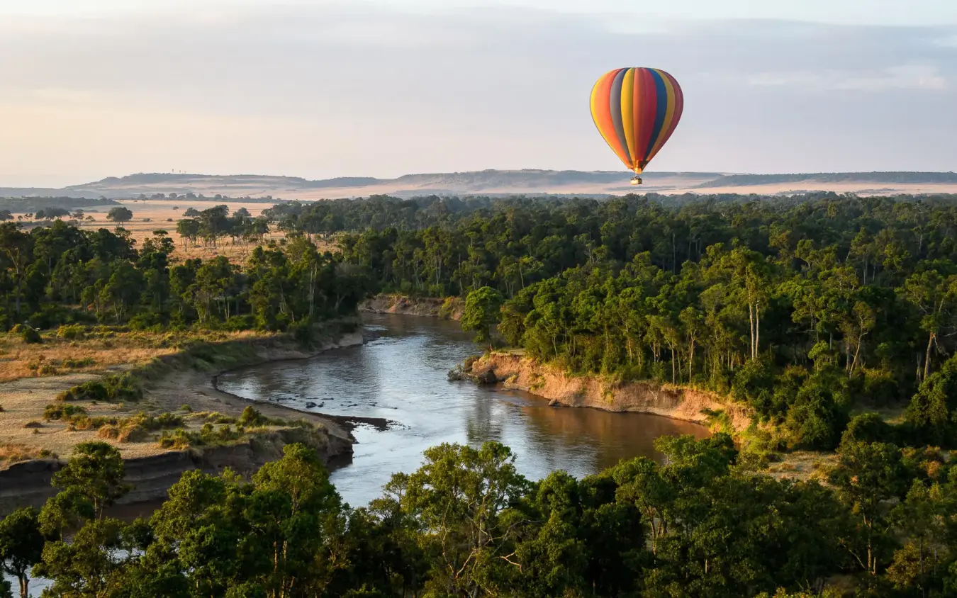 Hot air balloon floating over river and forested landscape, Offbeat Mara, Maasai Mara, Kenya