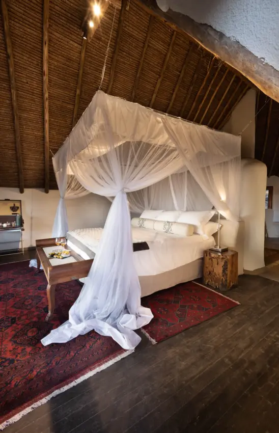 Canopy bed with white drapes in luxury bedroom with wooden ceiling, Ol Donyo Lodge, Amboseli and Chyulu Hills, Kenya