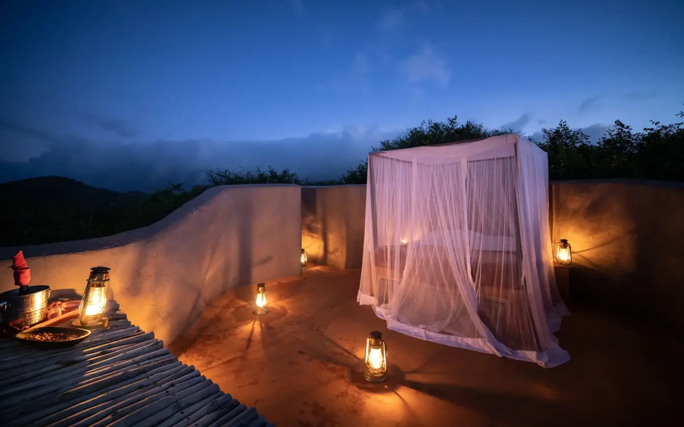 Luxury desert glamping setup with illuminated pavilions and fire pit at dusk, Ol Donyo Lodge, Amboseli and Chyulu Hills, Kenya
