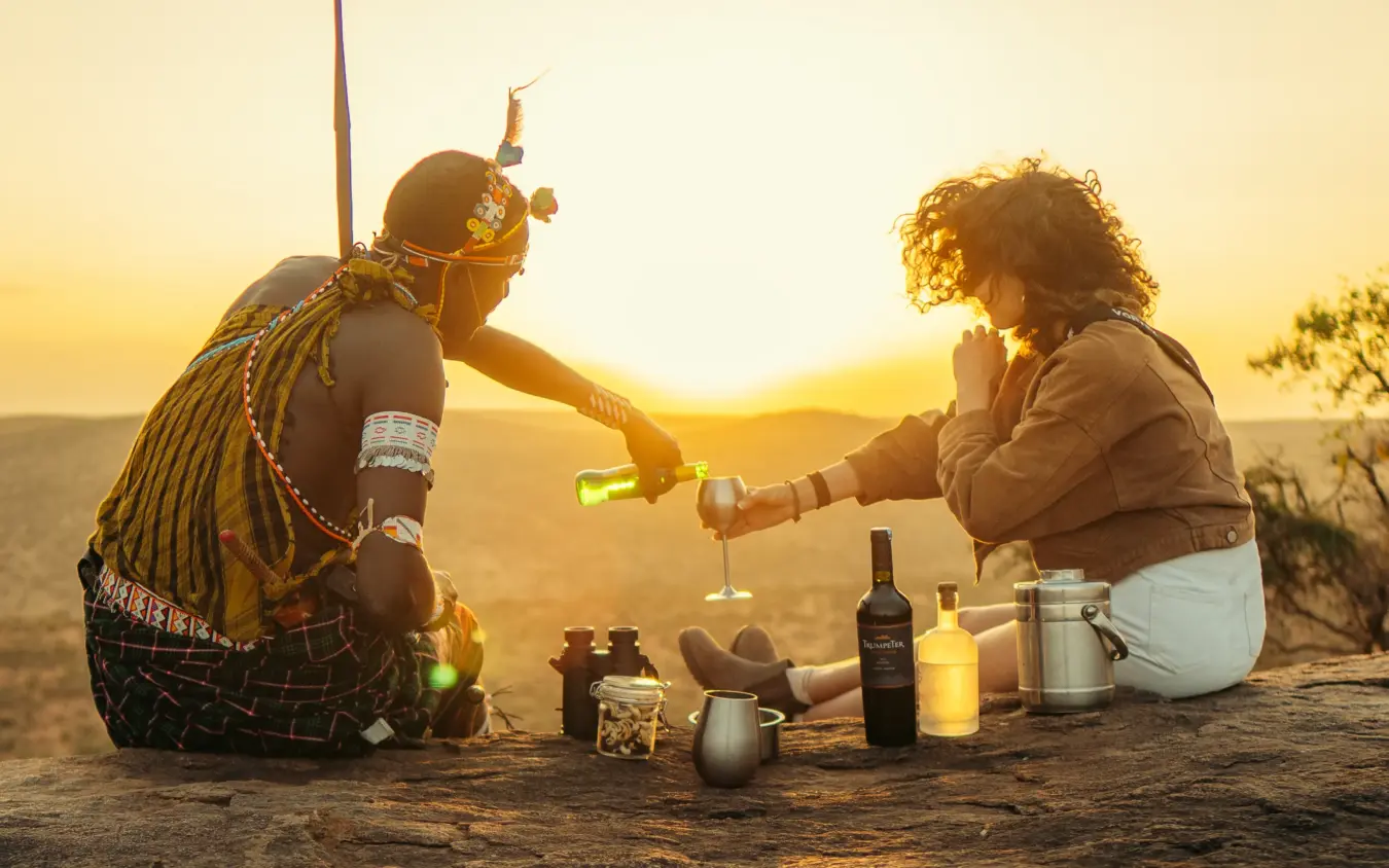 Two people toasting with drinks at sunset on rocky terrain overlooking savanna, Ol Malo House, Laikipia Highlands, Kenya