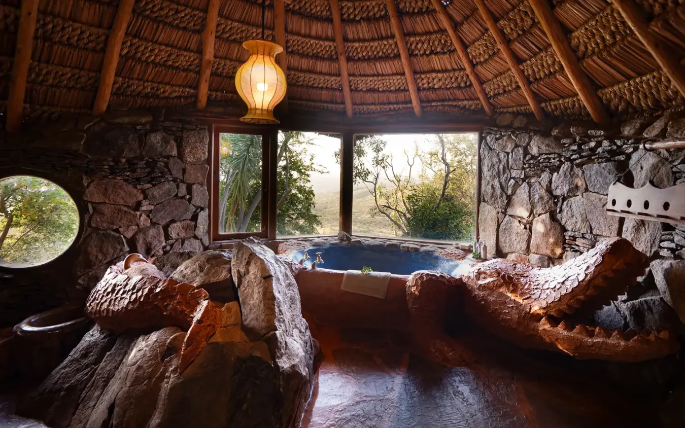 Rustic bathroom with wooden soaking tub and natural stone walls overlooking savanna, Ol Malo House, Laikipia Highlands, Kenya