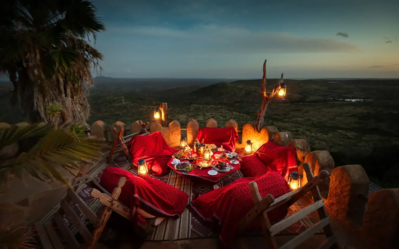 Outdoor dining setup with red fabrics and lanterns overlooking vast savanna landscape at dusk, Ol Malo House, Laikipia Highlands, Kenya