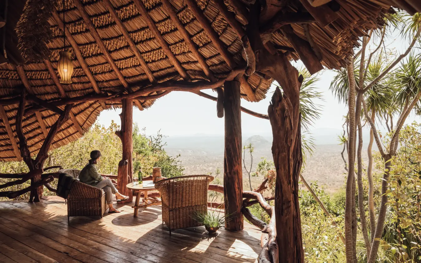 Guest relaxing on thatched pavilion deck overlooking vast landscape valley, Ol Malo House, Laikipia Highlands, Kenya