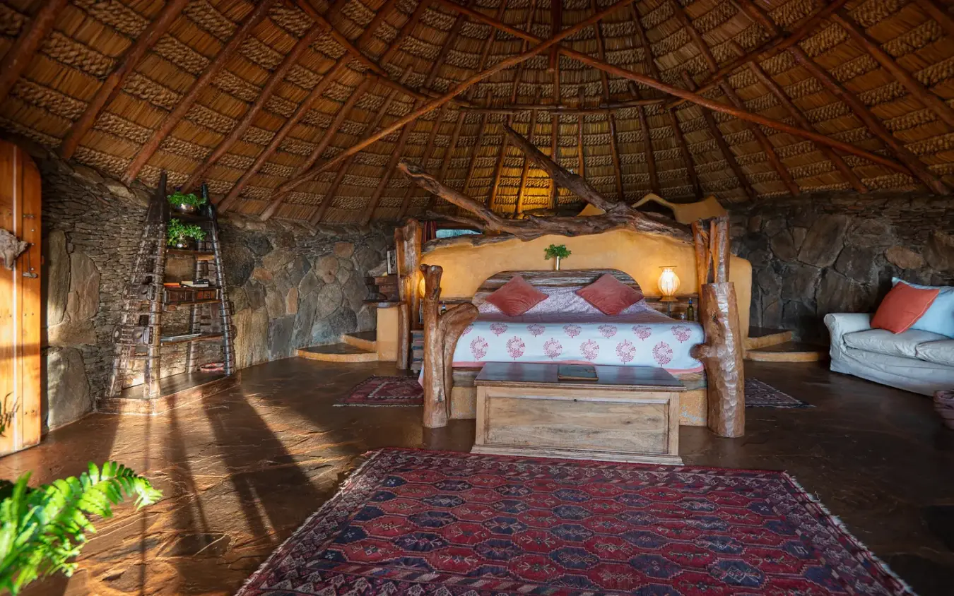 Thatched safari lodge interior with wooden bed and stone walls, Ol Malo House, Laikipia Highlands, Kenya