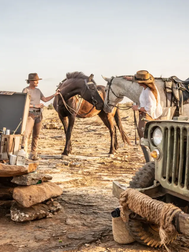 Cowboys with saddled horses and vintage jeep at desert camp at sunset, Ol Malo Lodge, Laikipia Highlands, Kenya