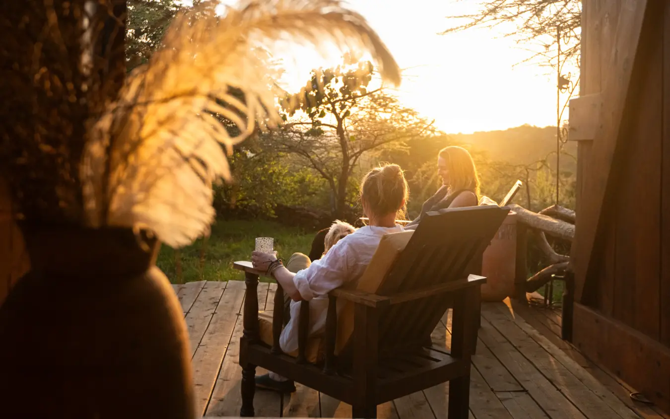 Guests relaxing in chairs on wooden deck at sunset with savanna landscape, Ol Malo Lodge, Laikipia Highlands, Kenya