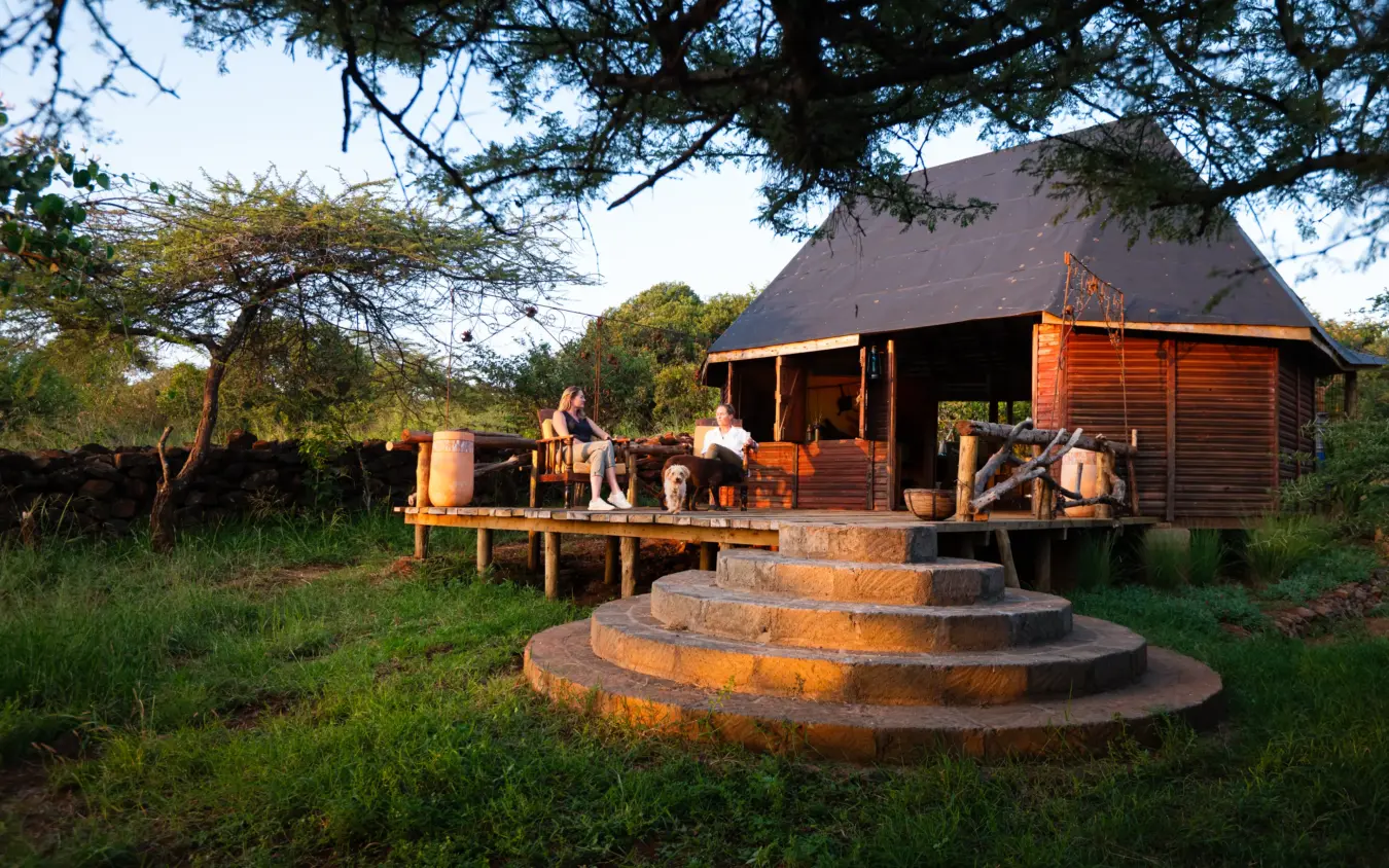Wooden lodge with circular stone firepit at dusk in bushland setting, Ol Malo Lodge, Laikipia Highlands, Kenya