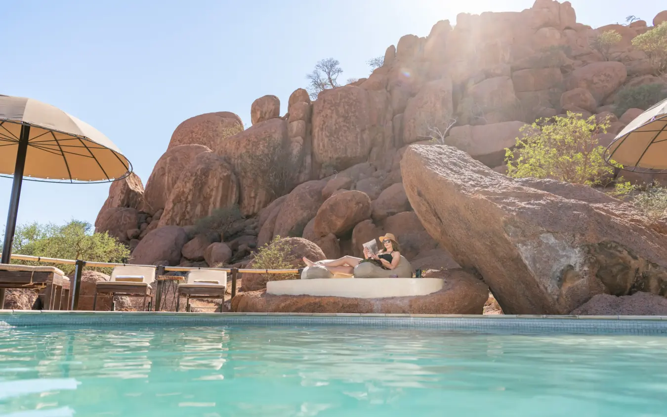Swimming pool with granite rock formations and lounge umbrellas, Onduli Ridge, Damaraland, Namibia