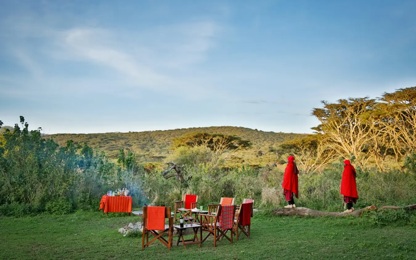 Maasai warriors in red robes standing near outdoor dining setup on grassland, Osonjoi Lodge, Ngorongoro Crater, Tanzania